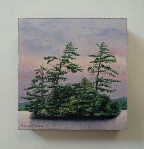 A watercolor painting of a small island with tall green pine trees under a soft pink, purple, and blue sky, with calm water in the foreground. Titled Evening Magic by Karen Richardson
