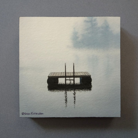 A serene watercolor painting of a small wooden raft floating on calm water, with soft gray-blue mist and trees in the background. Titled Lake Magic by Karen Richardson