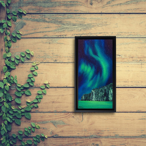 Framed artwork of the Northern Lights on a wooden wall with green leaves. Painting titled Mazinaw Marvel by Karen Richardson