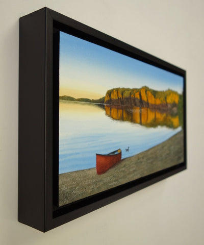 Framed painting of a red canoe on a beach with a scenic landscape of cliffs and water. Titled Mazinaw Mirror by  Karen Richardson