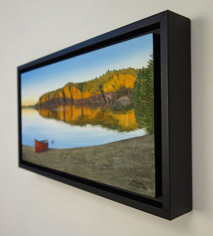 Framed painting of a red canoe on a beach with a scenic landscape of cliffs and water. Titled Mazinaw Mirror by  Karen Richardson