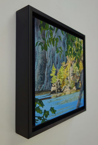 Framed scenic landscape with trees, rocks, and a blue lake. Titled Mazinaw Moment by Karen Richardson