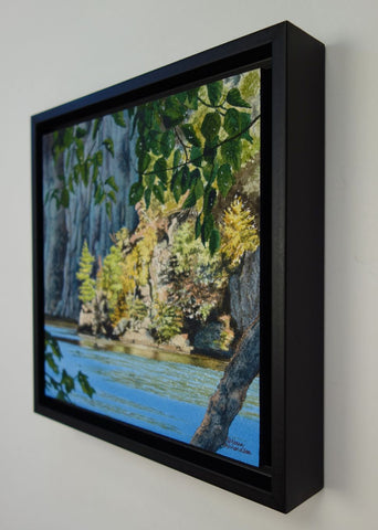 Framed scenic landscape with trees, rocks, and a blue lake. Titled Mazinaw Moment by Karen Richardson