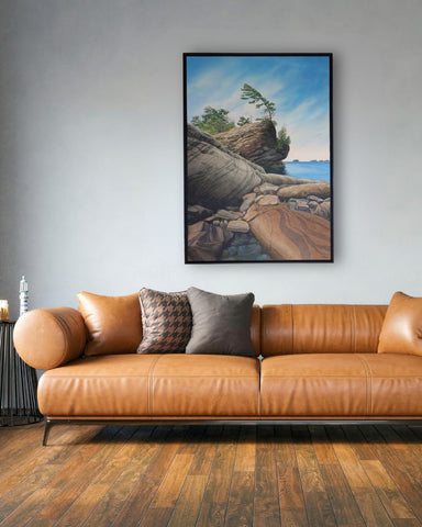 Brown leather sofa with decorative pillows in a room with a large framed painting of a Georgian Bay landscape on the wall, titled Serenity in Stone by Karen Richardson