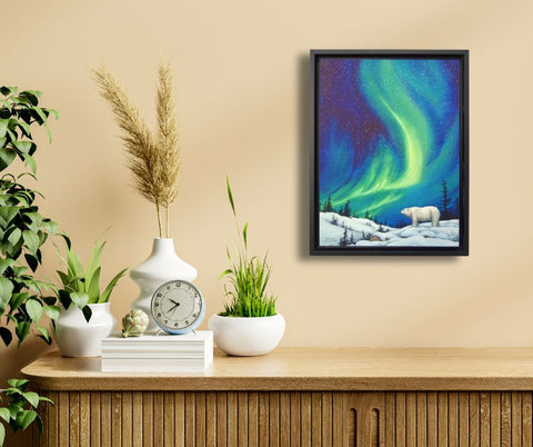 Framed artwork of a polar bear under the Northern Lights, titled Guardian of the Night, by Karen Richardson, shown on a wall above a wooden cabinet with decorative items.