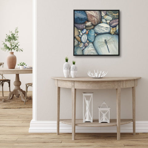 Framed painting of a dragonfly and pebbles titled Love Changes Everything, by Karen Richardson, shown above a wooden console table.