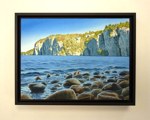 Framed painting of a lake with rocky shore and cliffs in the background. Titled Mazinaw Morning by Karen Richardson