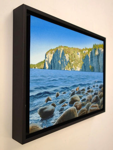 Framed painting of a lake with rocky shore and cliffs in the background. Titled Mazinaw Morning by Karen Richardson