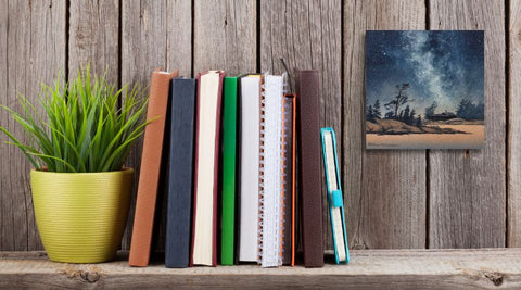 Painting of a starry night sky over a silhouette of trees and a cabin, titled Finding Peace, by Karen Richardson, shown in a home office setting.