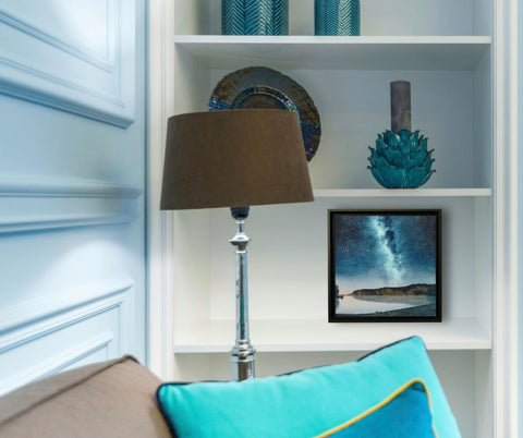 Painting of a starry night sky over a lake with cliffs and trees, titled Mazinaw Midnight, by Karen Richardson displayed in a living room setting.