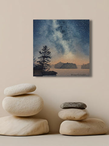Painting of a starry night sky over a lake with silhouetted trees, titled Stardust, by Karen Richardson, shown above stacked stones on a shelf.